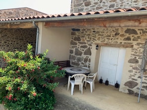 A stone building with a tiled roof, a white door, and a small patio area with a table and chairs. - Holiday Home Saint-beauzire Near Pauillac Castle (Saint-Beauzire)