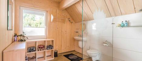 A wooden interior with a window, a sink, a toilet, and a shelf with folded towels.