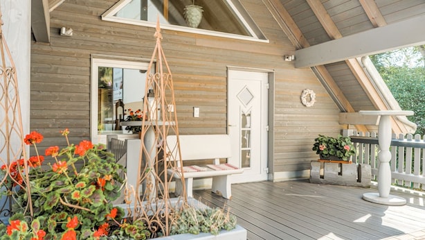 A wooden deck with a white bench, a hanging plant, and a view of the interior through a window.