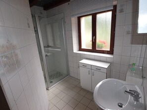 A bathroom with a glass shower enclosure, a sink with a mirror, and a window with frosted glass.