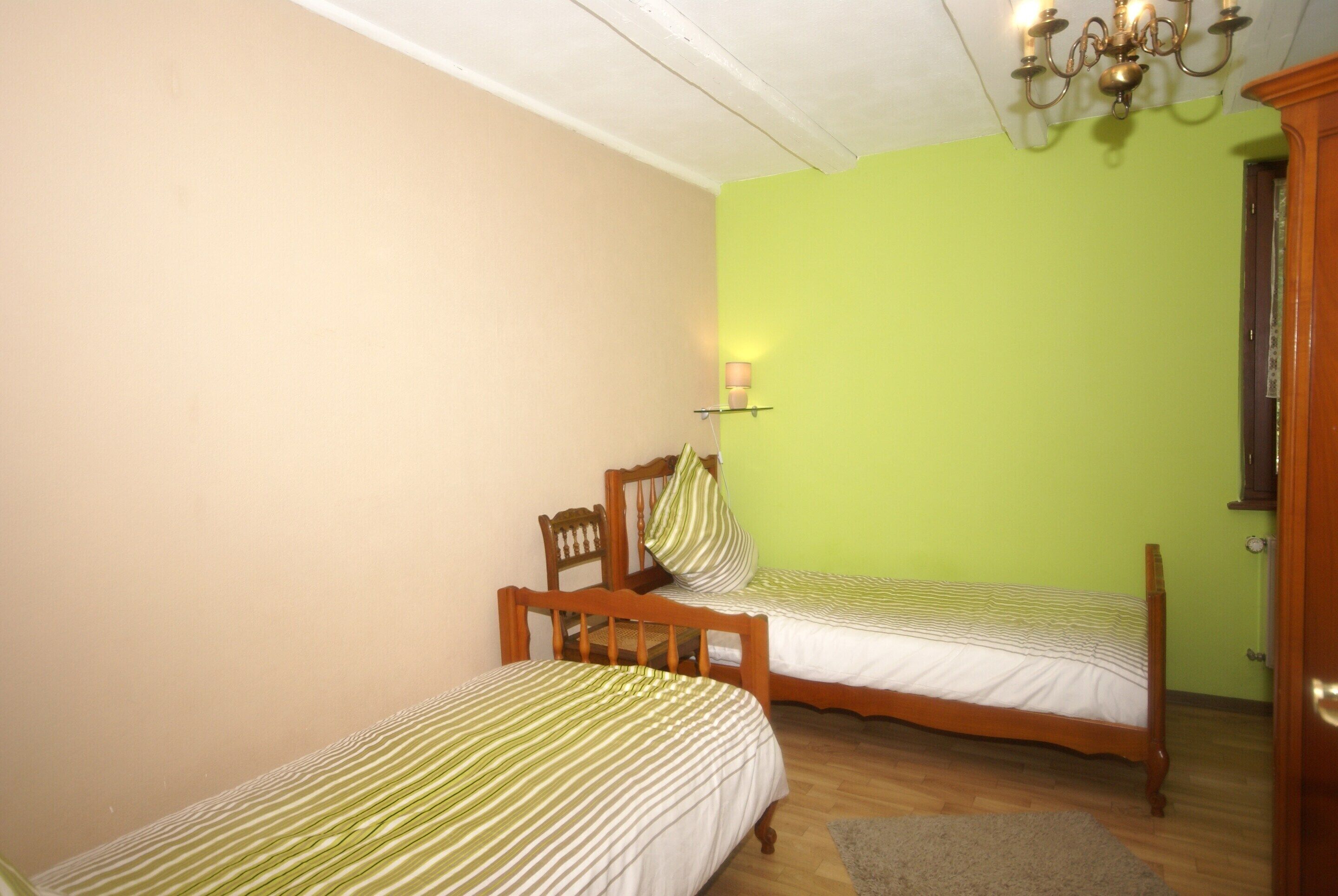 Une pièce avec deux lits en bois, un lustre et un mur vert.