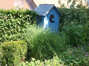 A blue mailbox with a birdhouse, surrounded by greenery and a building with a satellite dish. - Forest Retreat in Vosges (Hanviller)