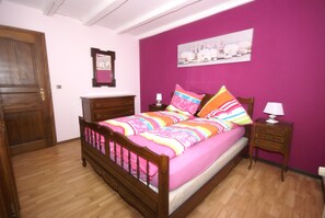 A bedroom with a wooden bed, a nightstand, a dresser, a door, and a wall with a picture. - Forest Retreat in Vosges (Hanviller)