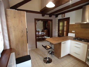 A kitchen with wooden cabinets, a gas stove, a sink, and a bar stool. - Forest Retreat in Vosges (Hanviller)