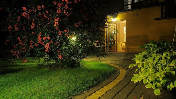 A paved pathway leading to a building entrance, surrounded by well-maintained grass and flowering bushes. - Hotel Arkadia (Plock)