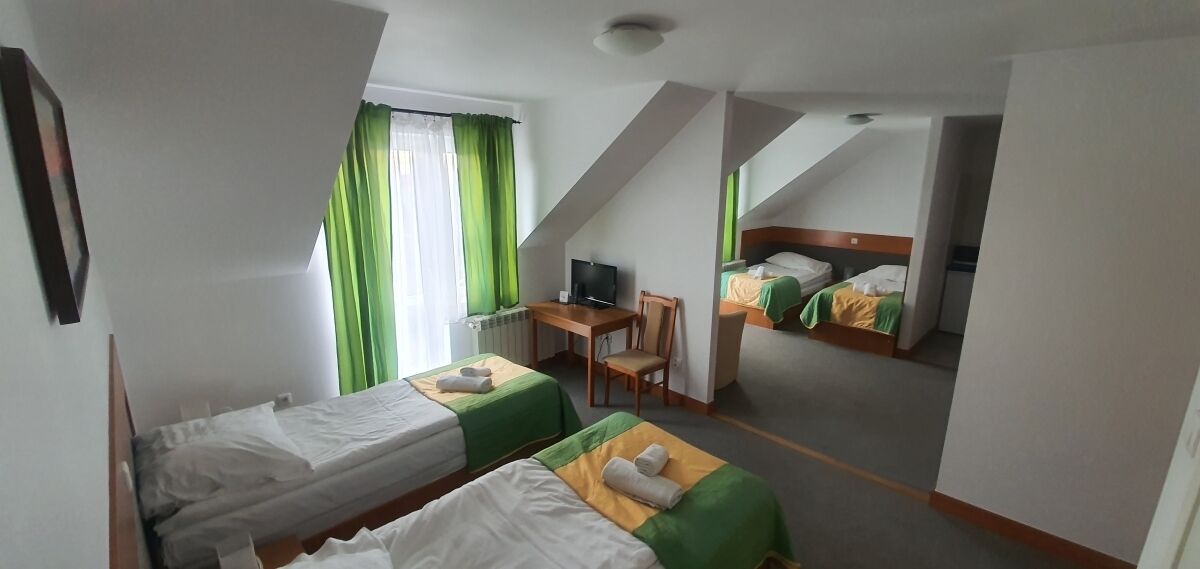 Een hotelkamer met twee eenpersoonsbedden, een bureau met stoel, een televisie en een raam met groene gordijnen.