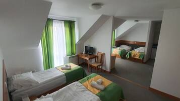 Een hotelkamer met twee eenpersoonsbedden, een bureau met stoel, een televisie en een raam met groene gordijnen.
