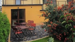 A multi-story building with balconies, a patio with outdoor furniture, and a garden with red flowers. - Hotel Arkadia (Plock)