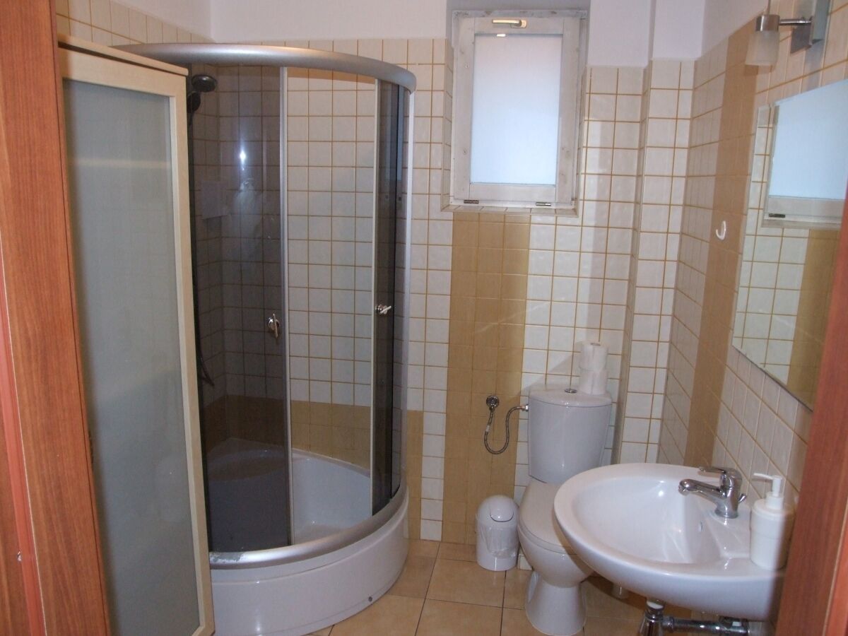A bathroom with a shower enclosure, toilet, sink, and a small window above the toilet.