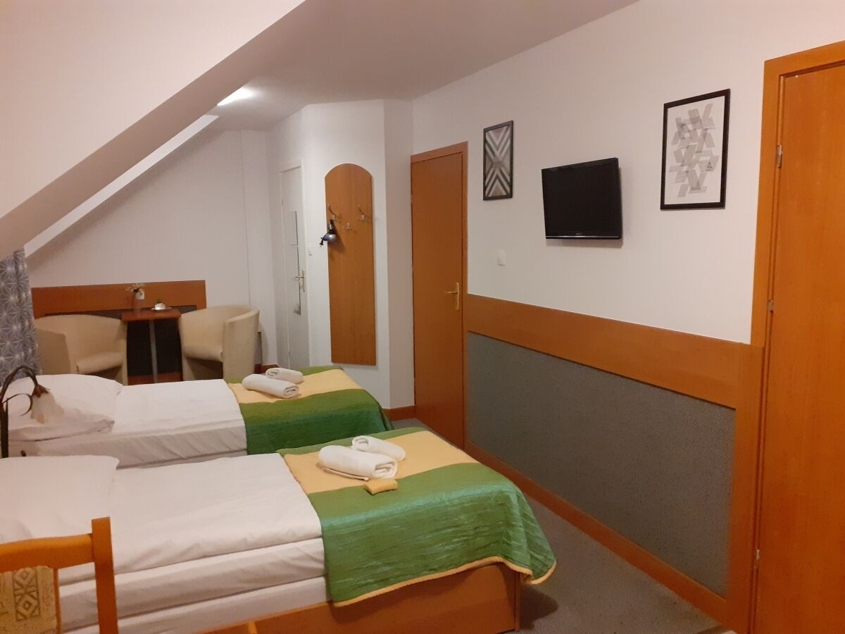 Una camera d'albergo con due letti singoli, una scrivania, una sedia, una televisione e una porta.