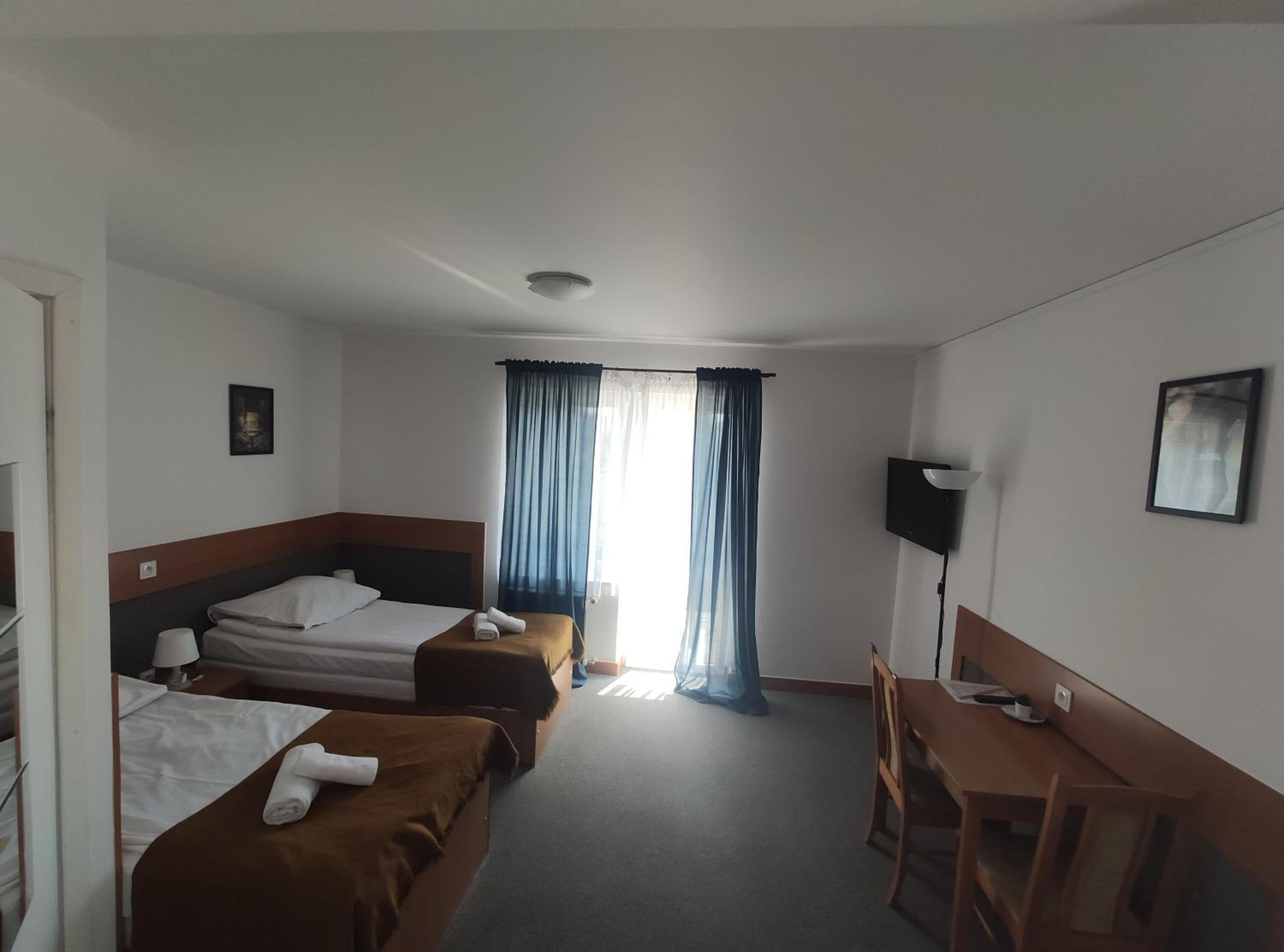 Habitación de hotel con dos camas, un escritorio, una silla, un televisor y una ventana con cortinas.