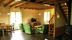 Un salon avec une cheminée, des fauteuils verts, une table à manger en bois et un téléviseur.