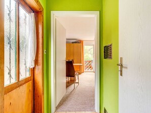 A hallway with a wooden door, a green wall, and a view into a dining area with a table and chairs.