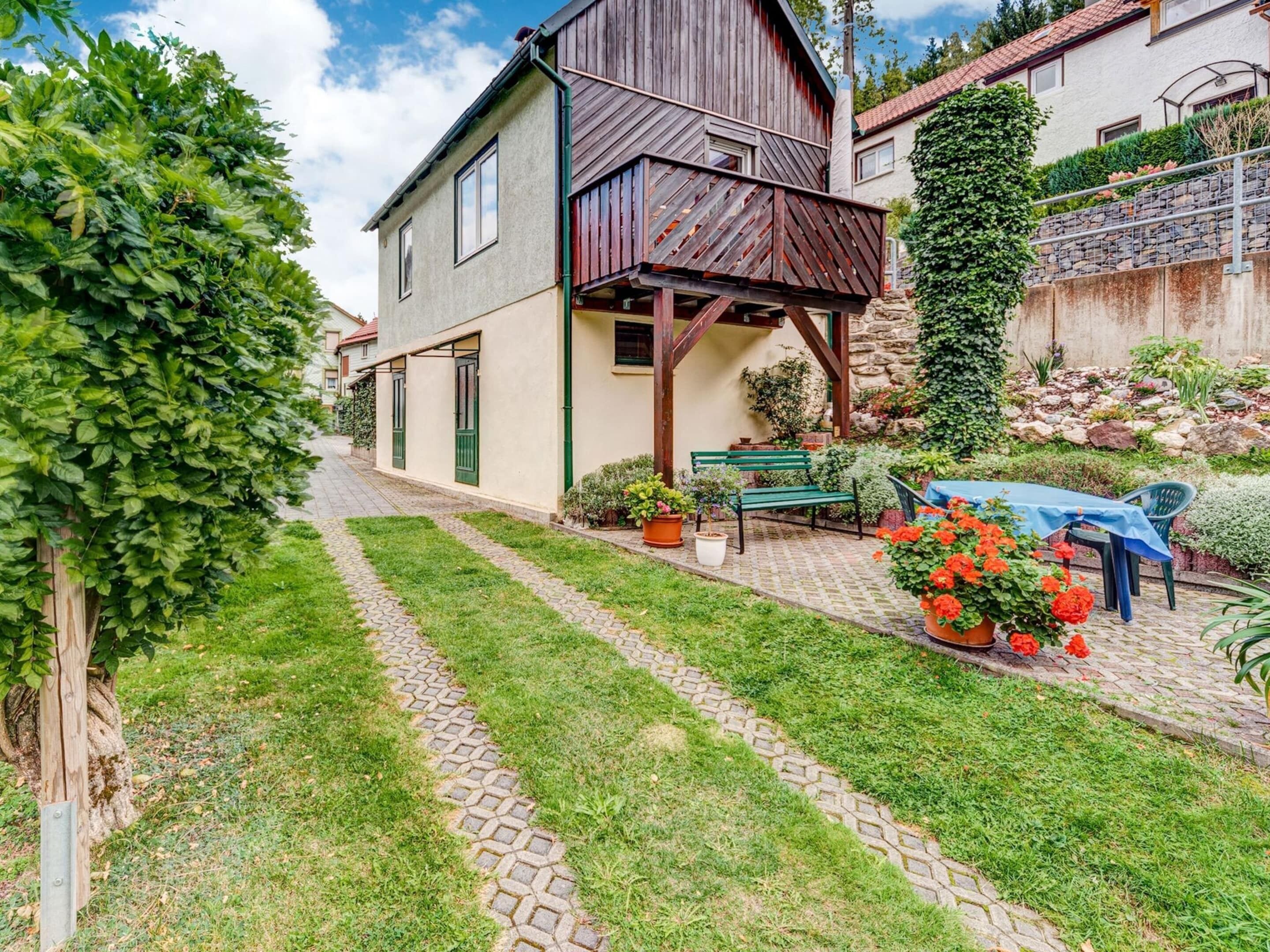 A house with a wooden balcony, a paved garden path, and a table with chairs.