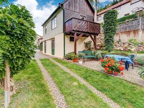 A house with a wooden balcony, a paved garden path, and a table with chairs.
