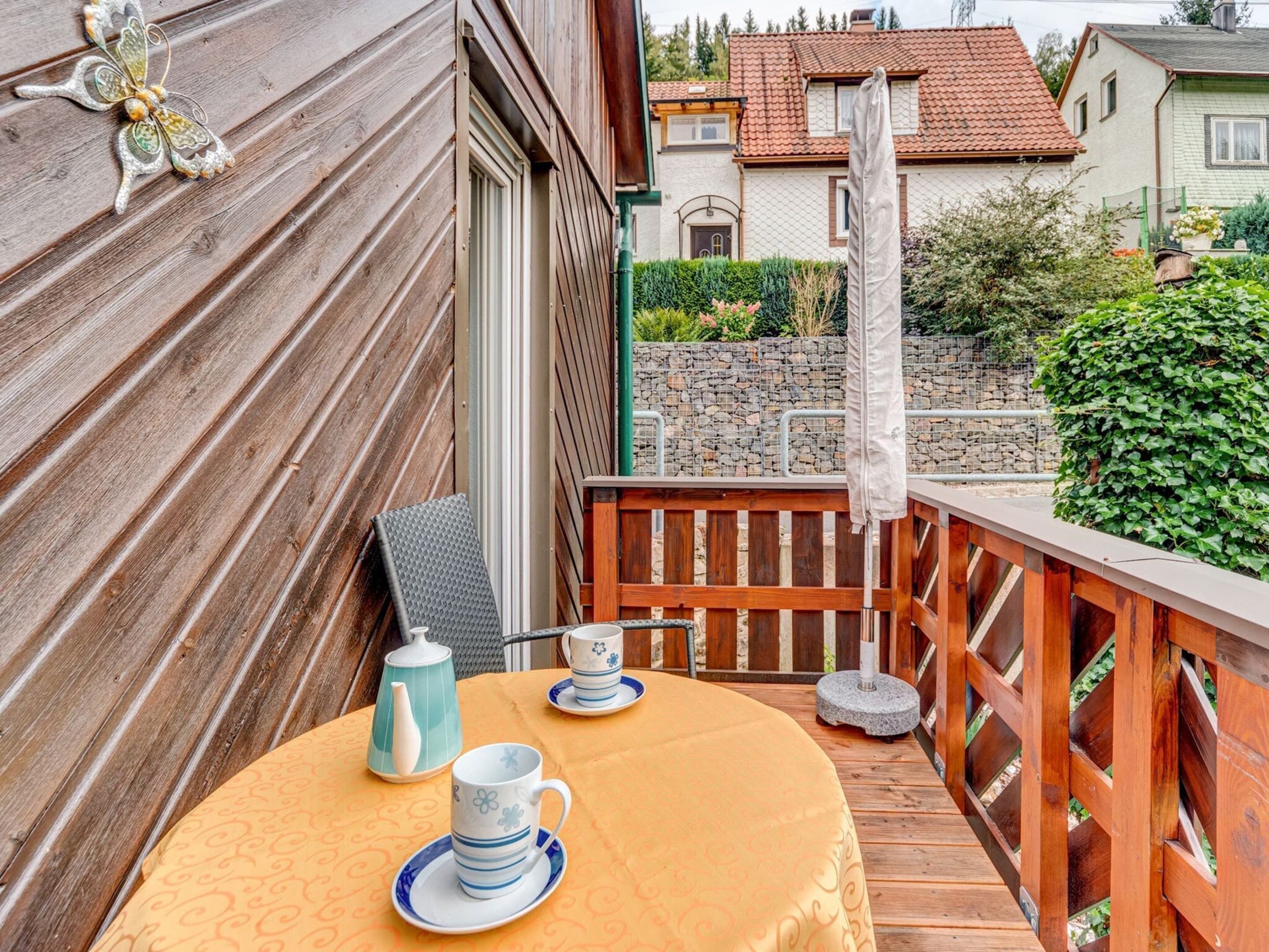 A wooden deck with a round table, two cups, a teapot, and a chair.