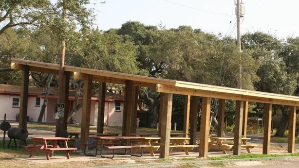 A wooden pavilion with picnic tables, a building in the background, and trees. - Bayfront Cottage Room 11 (Rockport)