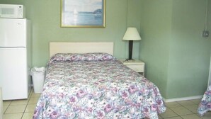 A bedroom with a bed, a nightstand, a lamp, a microwave, and a trash bin. - Bayfront Cottage Room 11 (Rockport)