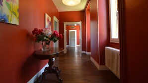 Un pasillo con paredes rojas, suelo de madera, una mesa con flores y una puerta al final.