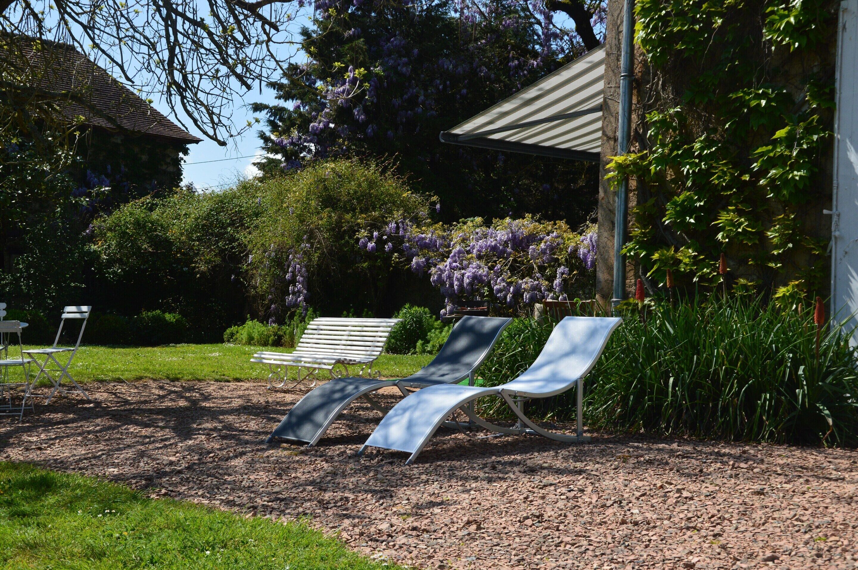 Un jardín con dos sillones de descanso, un banco y un edificio de techo inclinado.