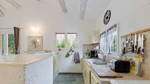 Eine Küche mit Steinfußboden, Holzbalken, einer Uhr und einem Fenster mit Vorhängen.
