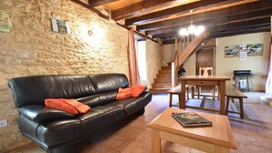 A stone-walled room with a black leather sofa, wooden table, and staircase. - Timeless Charm in Perigord (Saint-Leon-sur-Vezere)