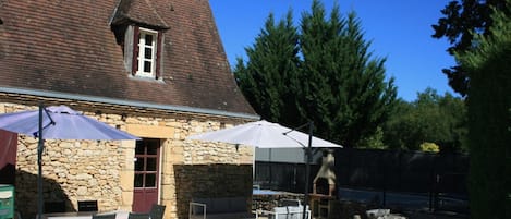 A stone building with a tiled roof, outdoor seating area, and a gravel courtyard.