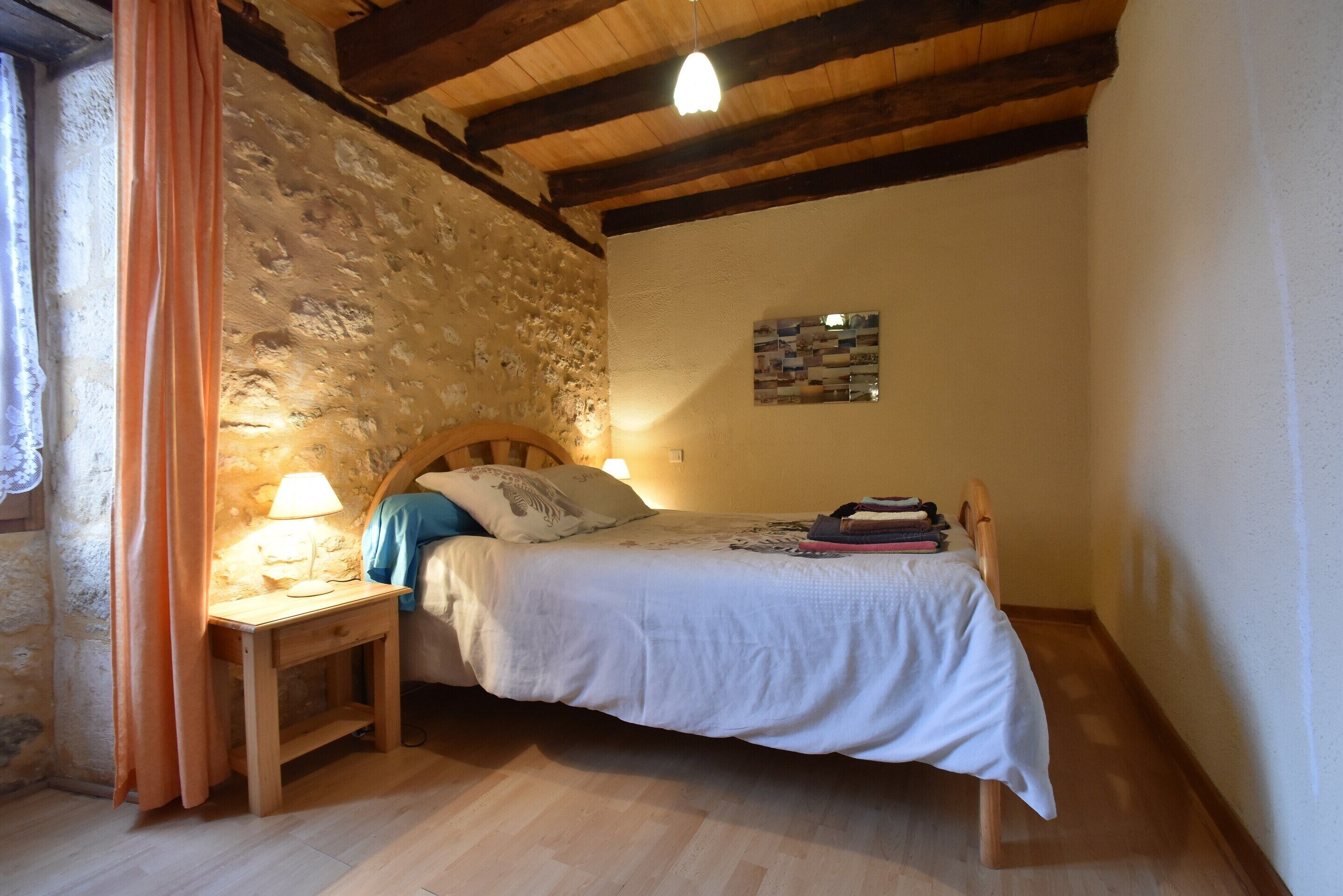 Una camera da letto con un letto di legno, un comodino, una lampada, un muro in pietra e un soffitto in legno.