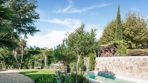 Une piscine entourée d’un mur de pierre, d’un chemin de gravier et de diverses plantes et arbres.