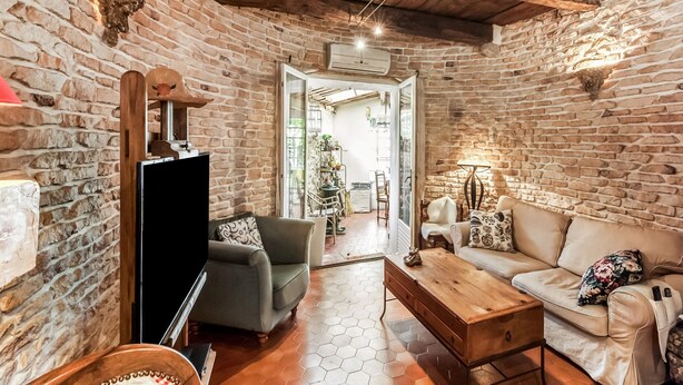 Un salon rustique avec des murs en pierre, un plafond en bois, un canapé, une table basse et un téléviseur.