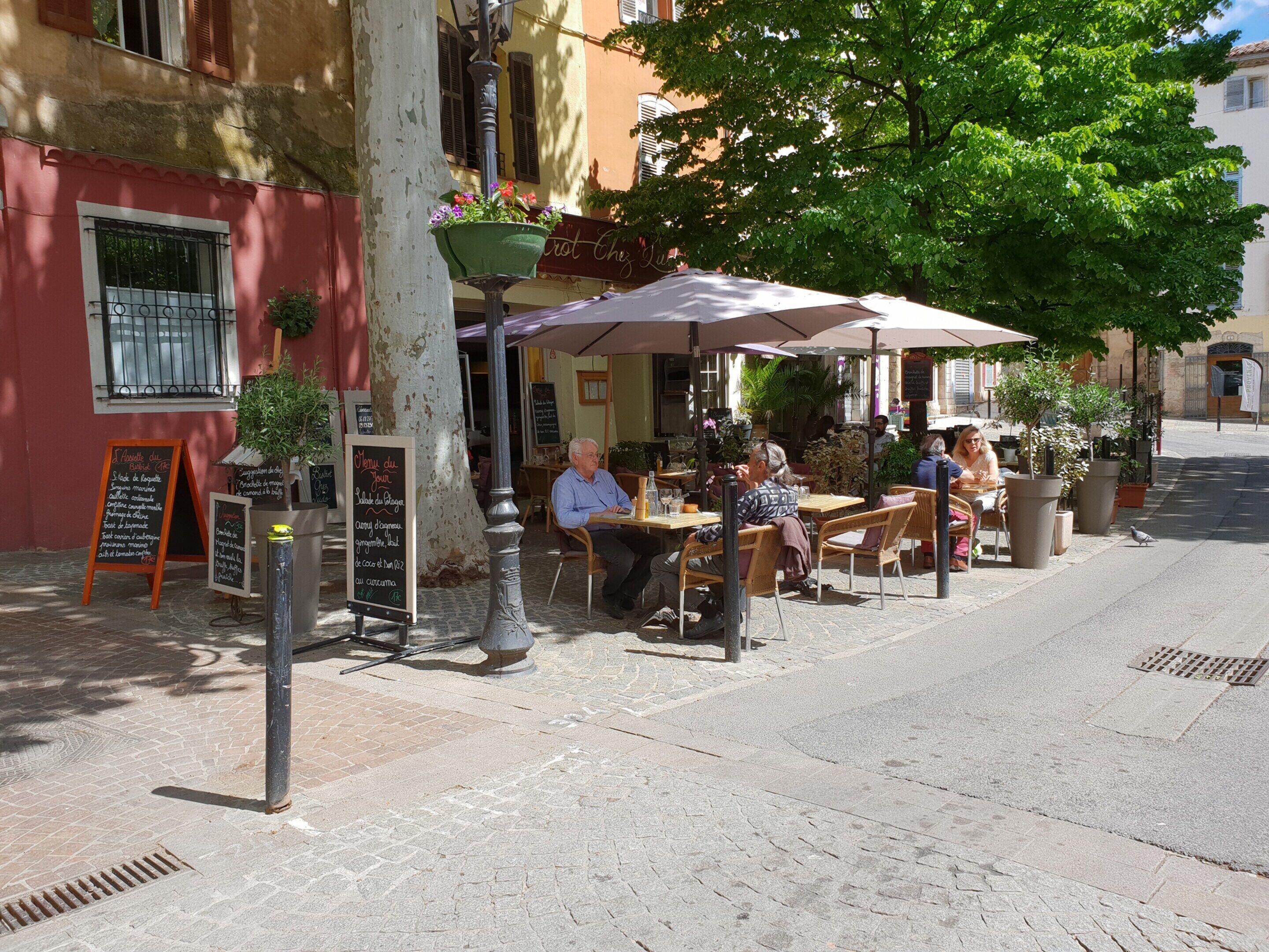 An outdoor café with tables and chairs, a street lamp, and a chalkboard menu.