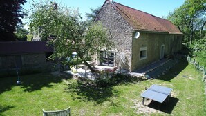 A stone building with a sloped roof, a small outdoor seating area with tables and chairs, and a solar panel. - Cottage in Wierre-effroy Near Forest (Wierre-Effroy)