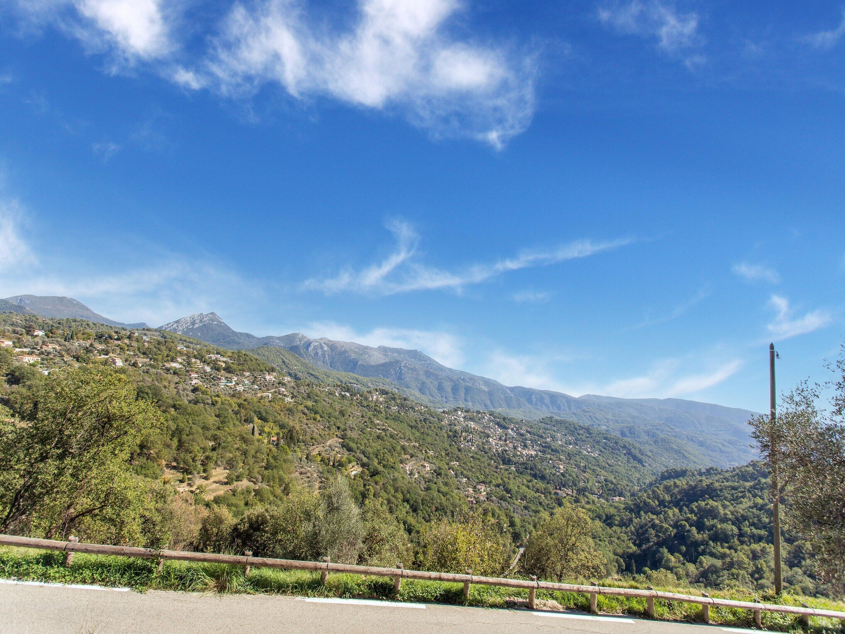 A road with a wooden guardrail, a clear blue sky, and a mountainous landscape with scattered buildings.