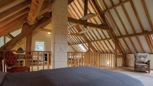 An attic bedroom with exposed wooden beams, a large bed, a chair, and a view of the outdoors. - Beautifully Located Country House With Heated Pool (Auriac)