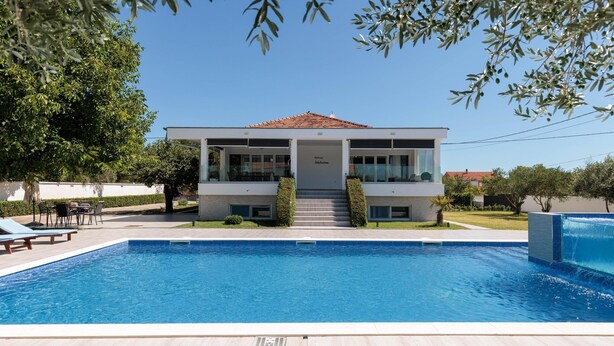 Uma casa moderna de dois andares com piscina em frente.