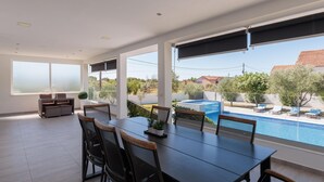 Uma área de refeições ao ar livre e espaçosa, com vista para a piscina, incluindo uma mesa e cadeiras, um pequeno espaço para sentar e a paisagem circundante.
