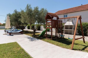 A residential outdoor area with a play structure, a covered seating area with lounge chairs, and a house with a tiled roof. - Holiday Home in Galovac With Pool (Galovac)