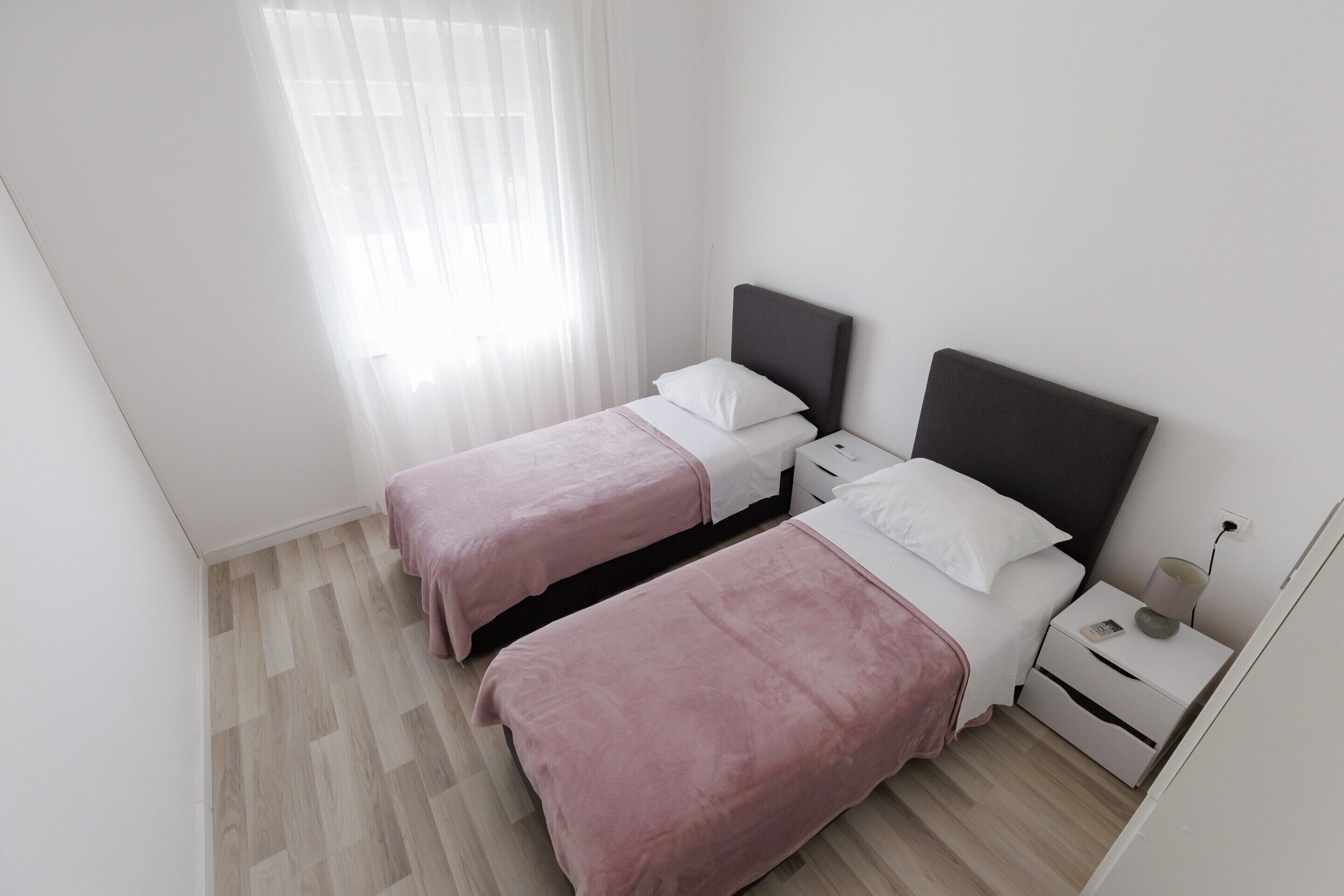 A twin room with two beds, a nightstand, a lamp, and a window with sheer curtains.