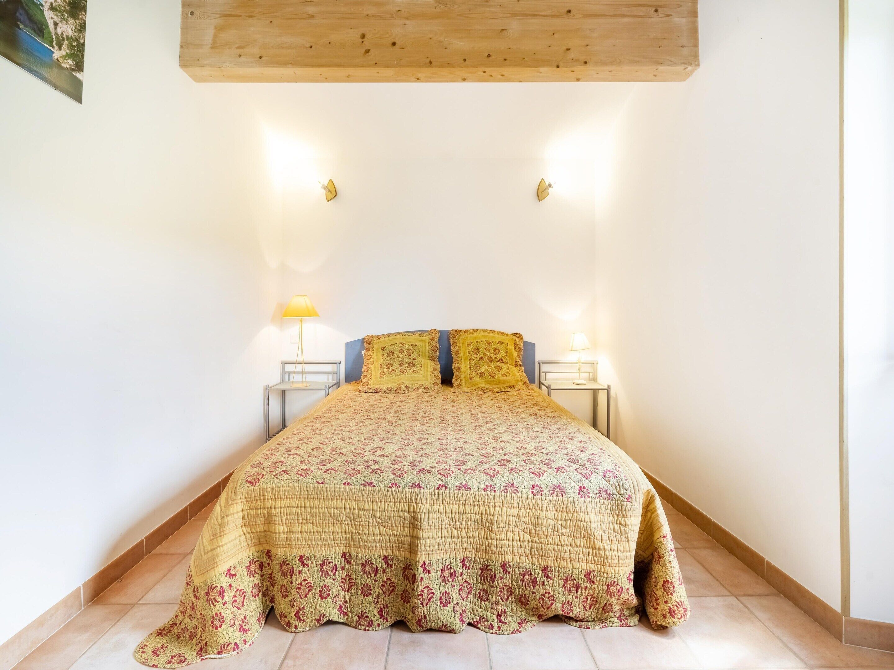 A bedroom with a bed, two bedside tables, a lamp, and a wooden ceiling.