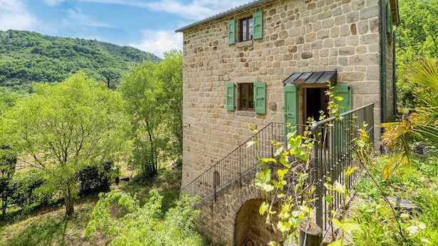 Kivinen rakennus, jossa on portaikko, ja sen ympärillä on vehreää kasvillisuutta ja kukkuloita.