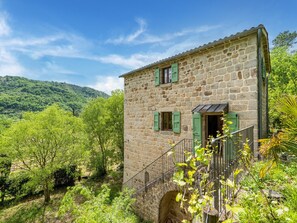 Un edificio in pietra con una scala, immerso nel verde e circondato da colline.