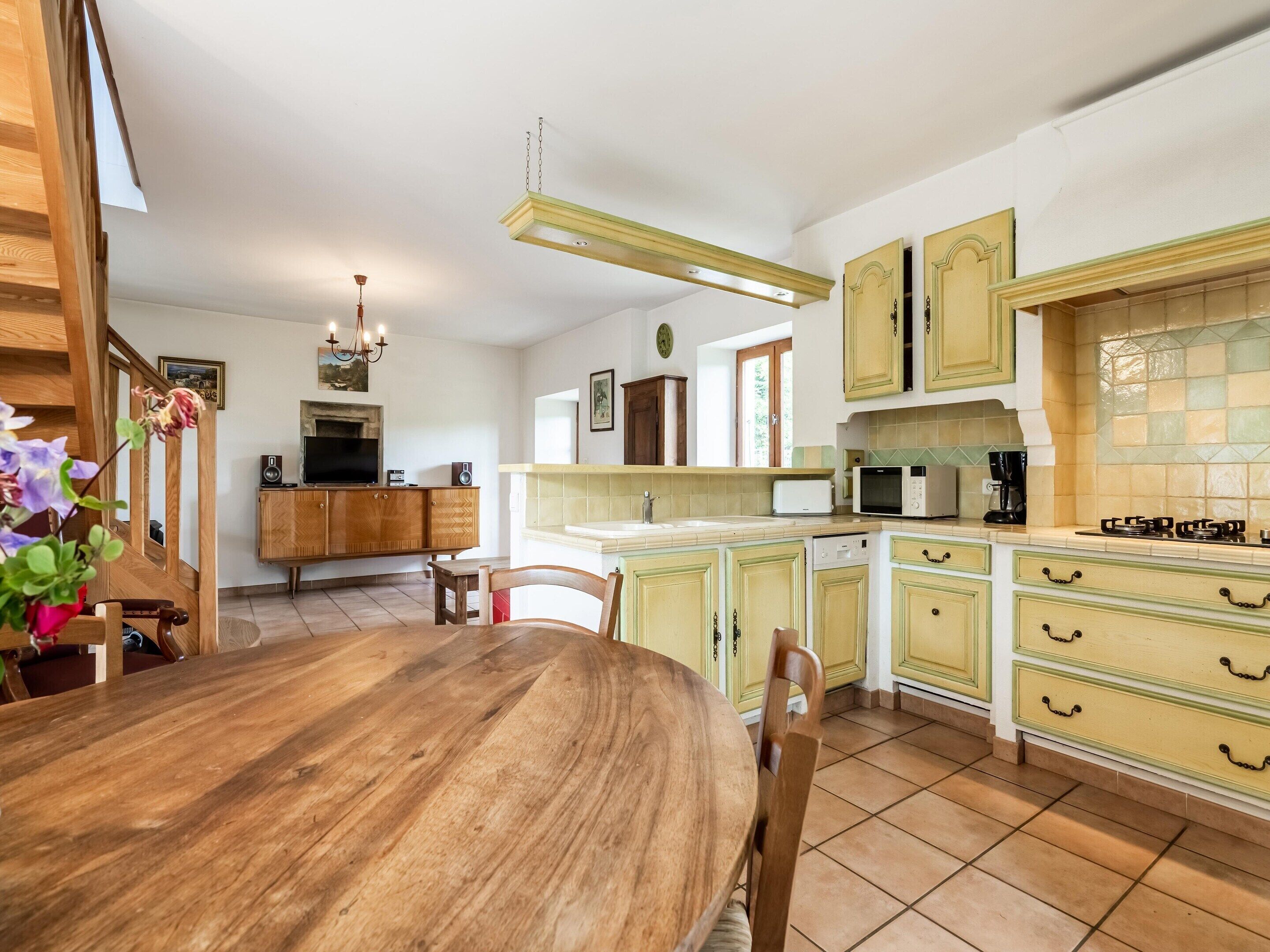 Una cocina con armarios de madera, una mesa de comedor, sillas, una lámpara colgante y vistas al área de estar.