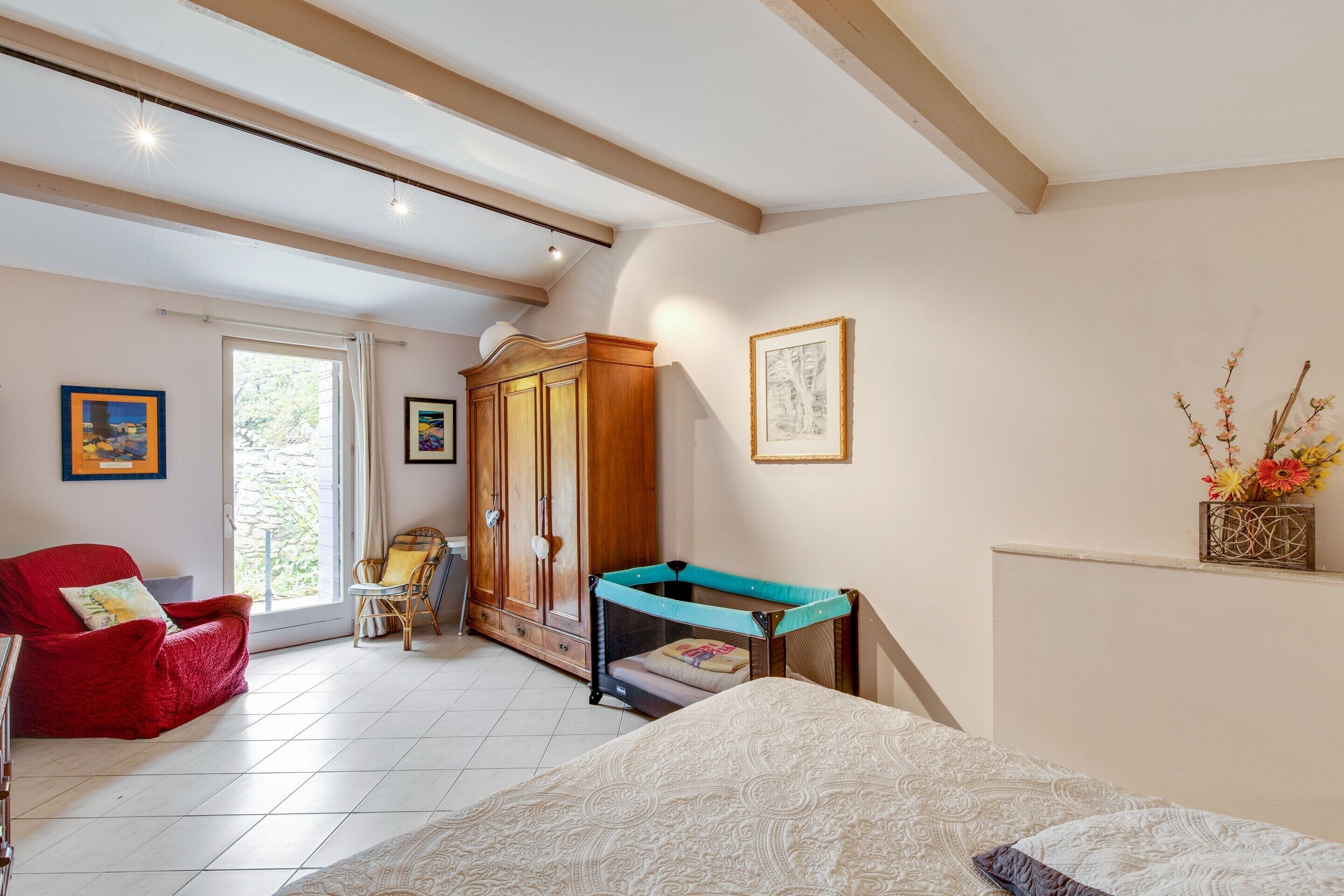 A bedroom with a bed, a red chair, a wooden wardrobe, and a window.