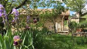 A stone house with a tiled roof, a stone porch, and a garden with purple flowers. - House in Ardeche Near Ray-pic Falls (Saint-Pierre-de-Colombier)