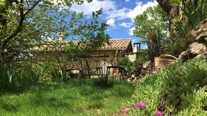 A garden with a stone building, metal chairs, and green plants. - House in Ardeche Near Ray-pic Falls (Saint-Pierre-de-Colombier)
