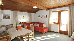 Ett mysigt vardagsrum med ett träpanelat tak, ett matbord med stolar, en röd soffa och ett fönster med gardiner.