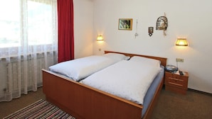 Ett hotellrum med en säng i trä, två sänglampor, ett nattduksbord och ett fönster med tunna, genomskinliga gardiner och en röd gardinkappa.