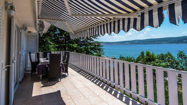 Ein überdachter Balkon mit Seeblick und Blick auf ferne Hügel.