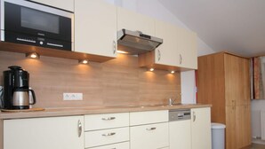 A modern kitchen with a microwave, coffee maker, and built-in oven. There are wooden cabinets and a dishwasher. - Stylish Flats in Uderns Near Ski Lift (Uderns)