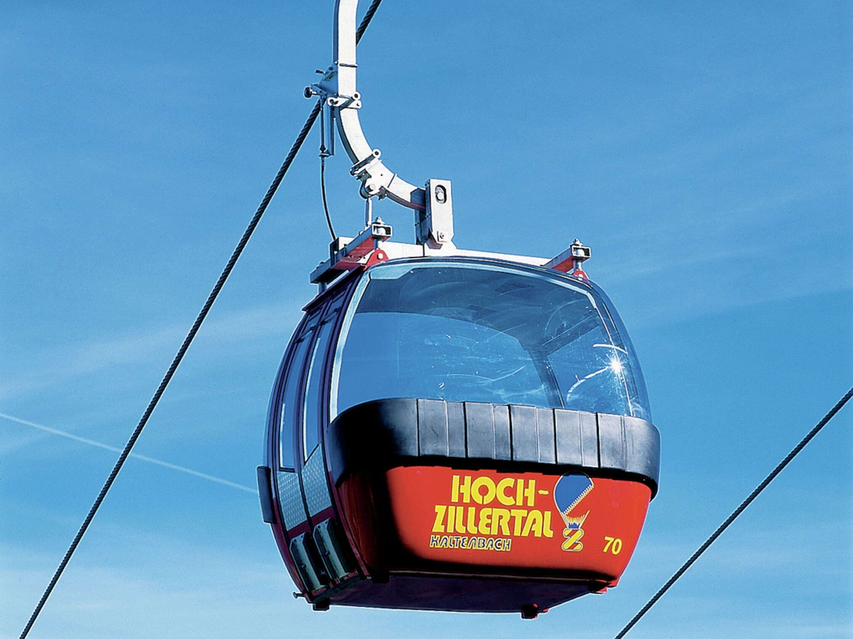 A cable car with "Hoch-Zillertal" and "70" on its side, suspended by cables against a clear sky.